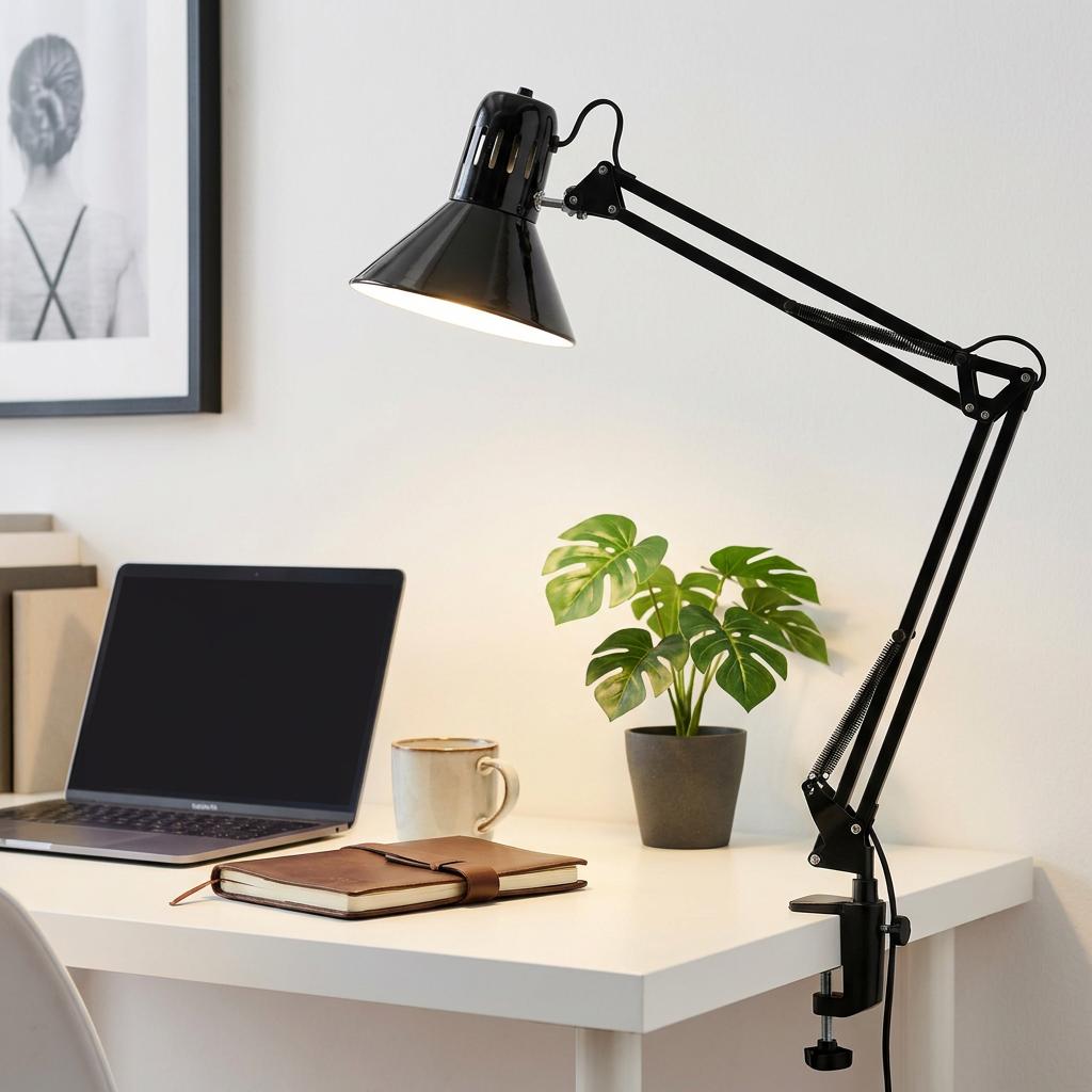 Black Eglo Firmo clip-on swing arm lamp illuminating a desk with a laptop, plant, and notebook.