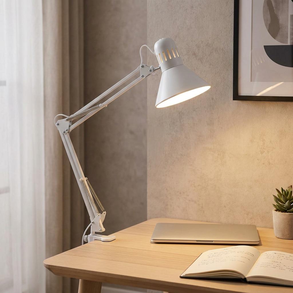 White adjustable clip-on desk lamp illuminated over a wooden desk with a laptop and notebook.