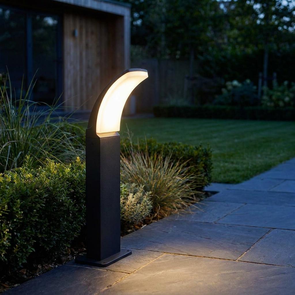 Eglo Fiumicino black LED bollard light with a curved glowing head beside a slate patio in a garden at dusk.