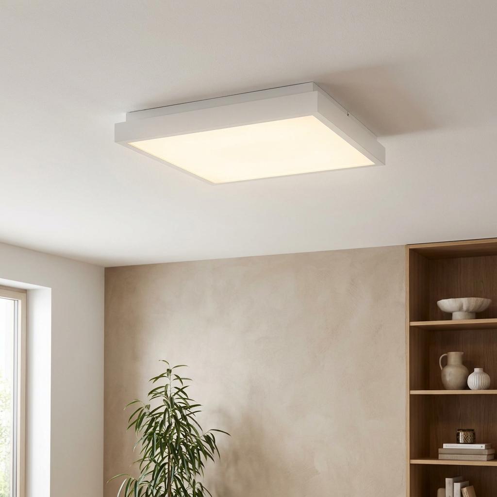 White square LED flush ceiling light glowing in a modern room with a green plant and wooden bookshelf.