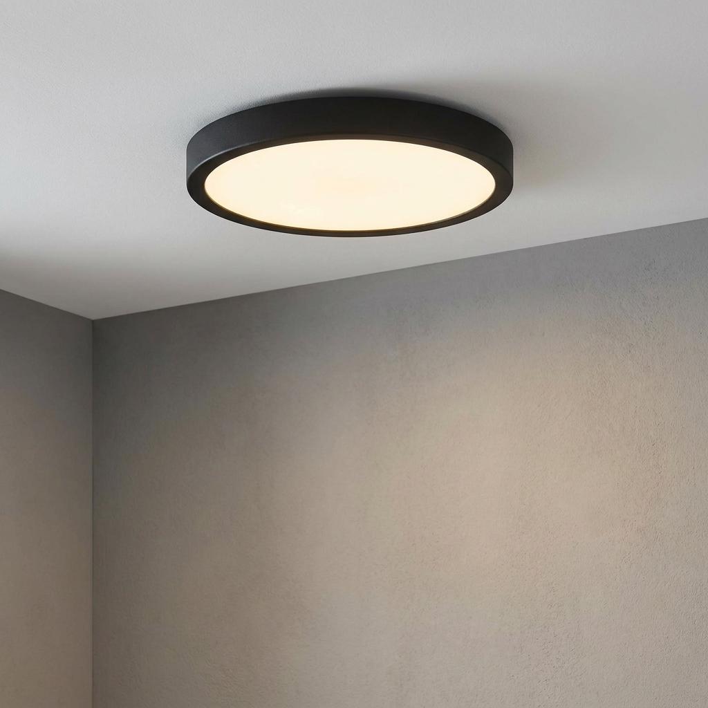 Circular black flush-mount LED ceiling light with a warm white diffuser against a grey textured wall.
