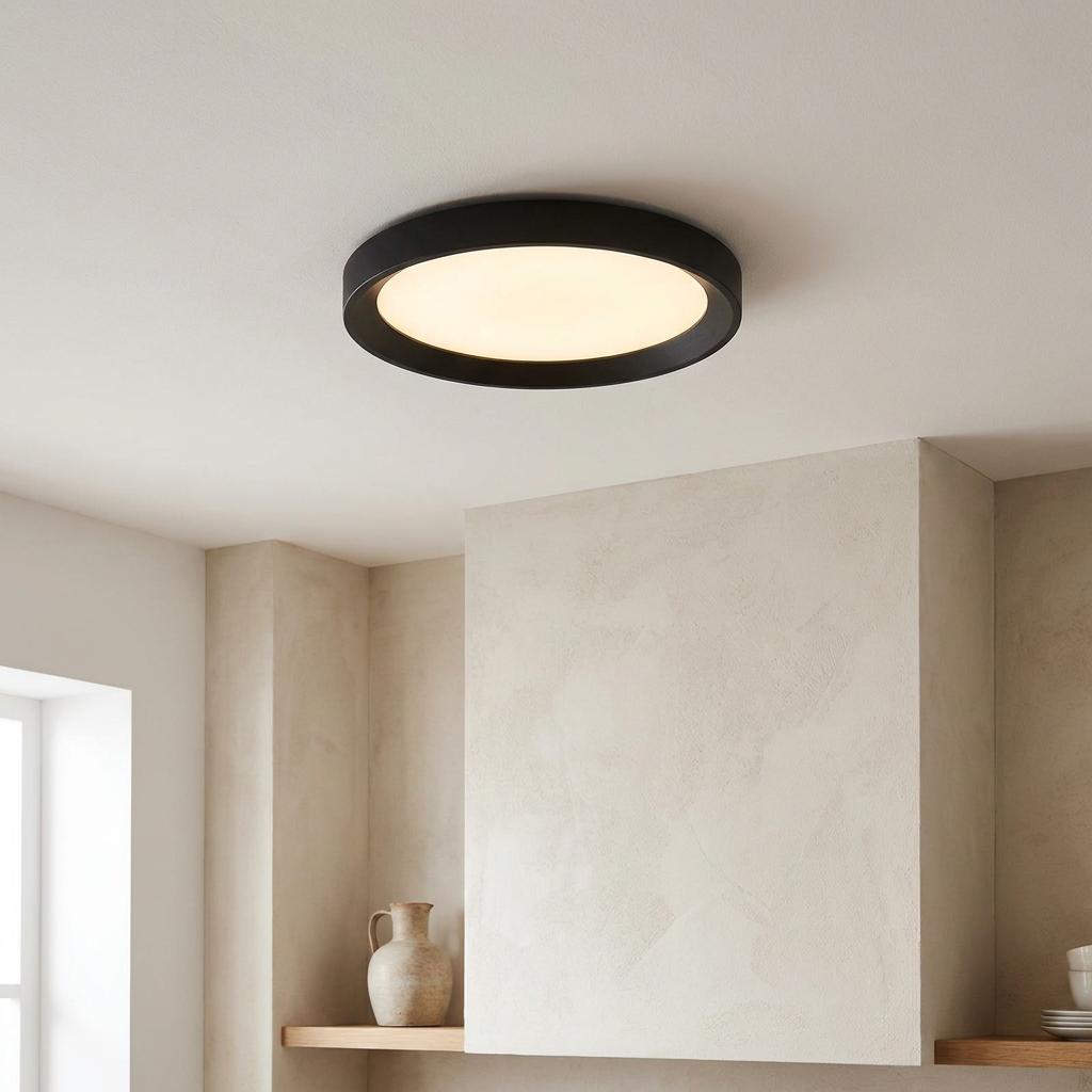 Round black flush ceiling light with warm white illumination mounted in a minimalist neutral interior.