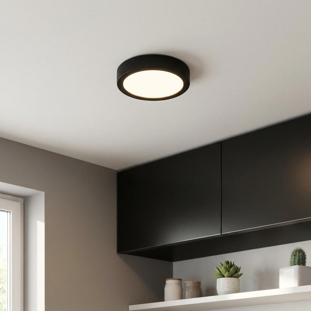 Modern round black flush ceiling light illuminating a minimalist room with dark cabinets.
