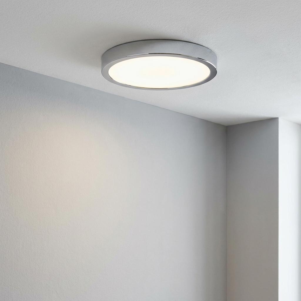 Round chrome LED flush ceiling light illuminated on a white ceiling.