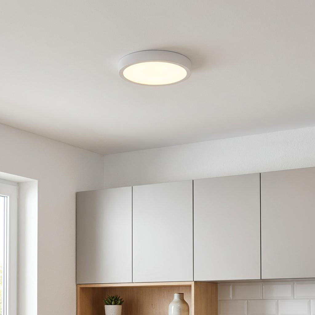 Round white flush LED ceiling light glowing in a minimalist kitchen above grey cabinets.