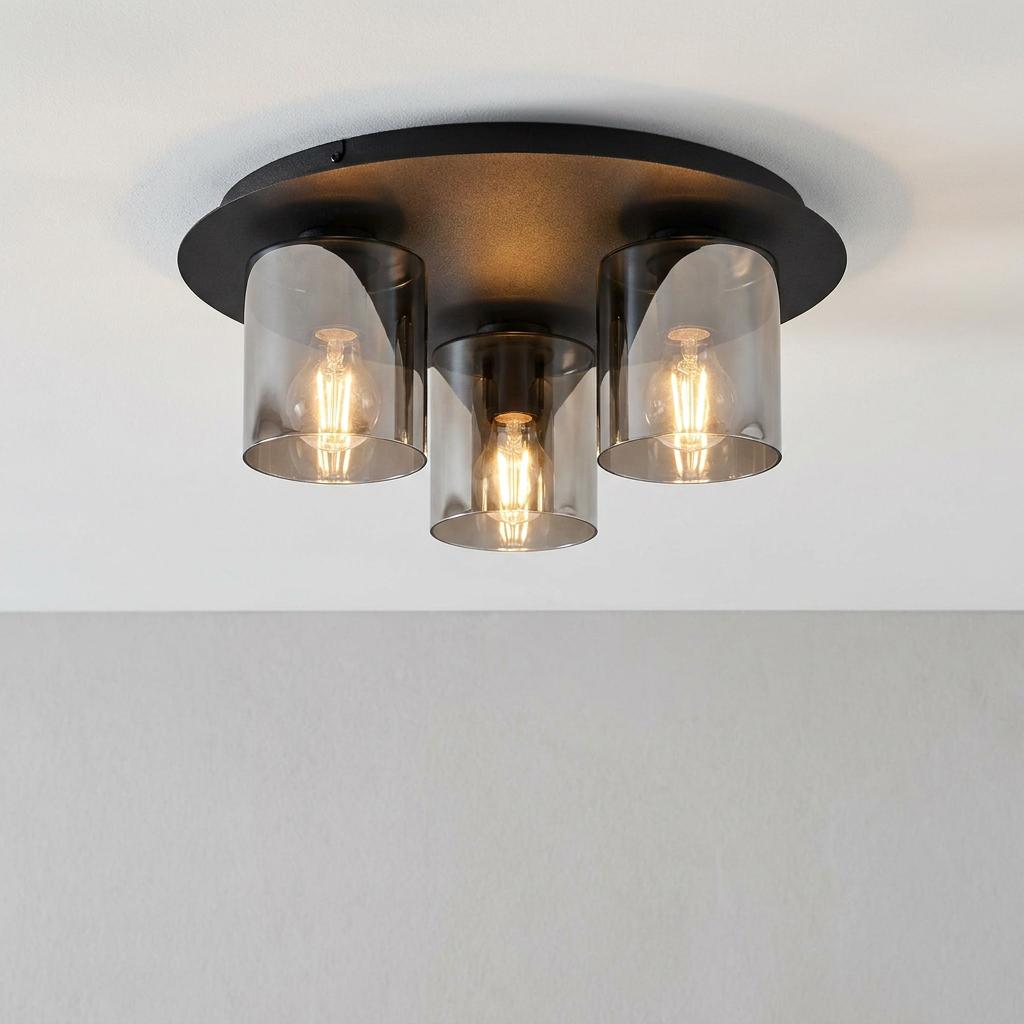 Black round ceiling flush light featuring three smoked glass cylindrical shades and warm filament bulbs.