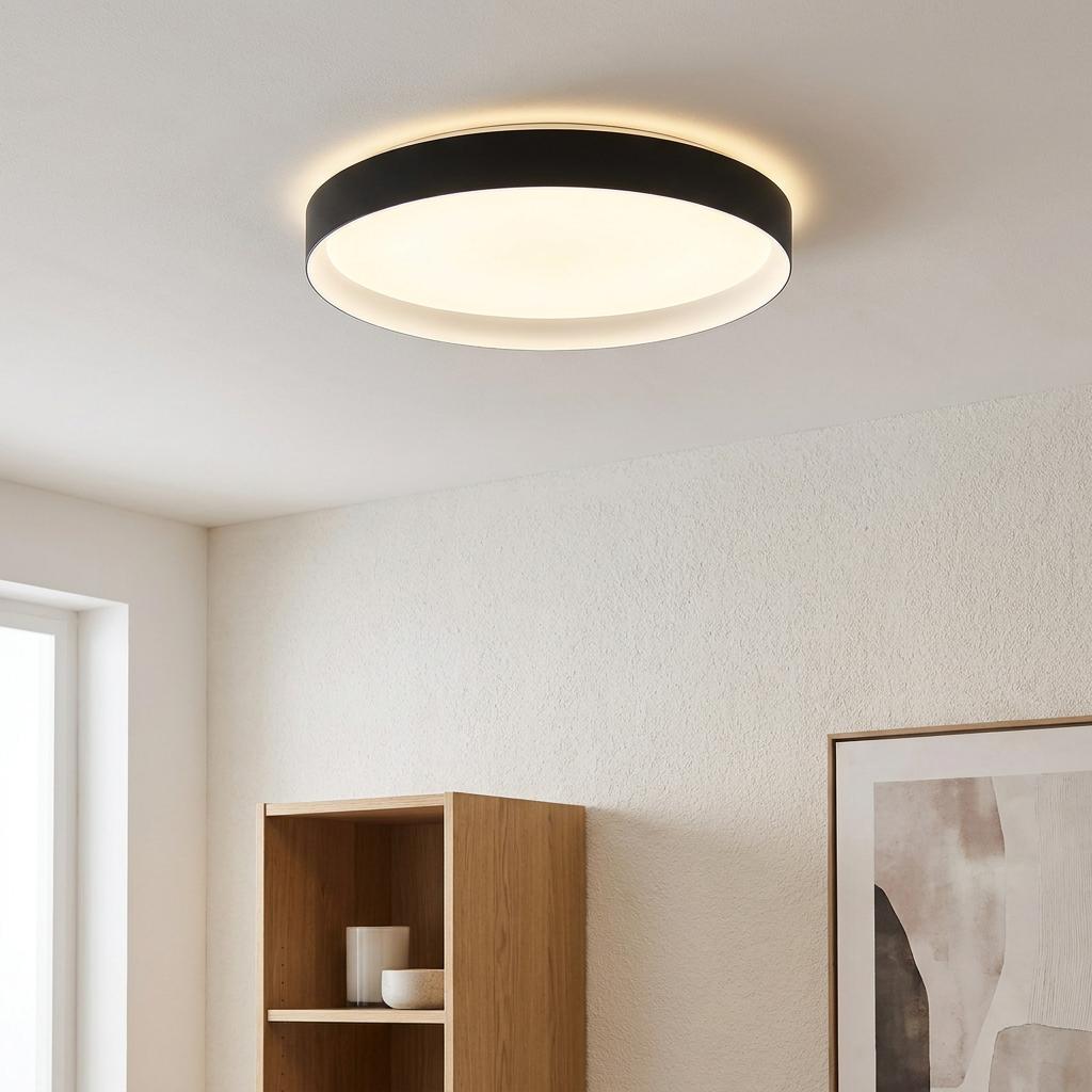 Circular black flush-mount LED ceiling light illuminated in a modern room above a wooden bookshelf.
