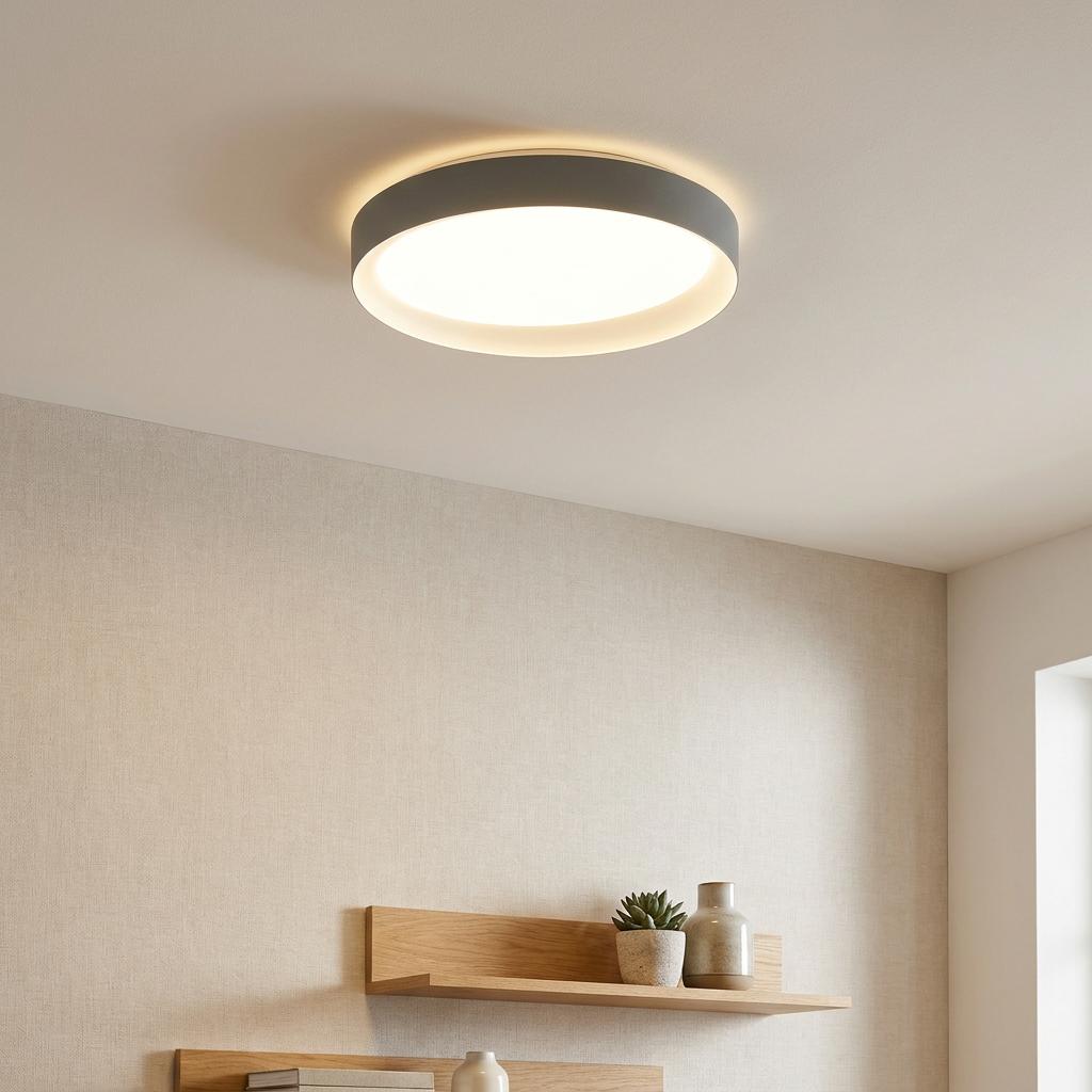 Grey circular LED flush ceiling light illuminating a minimalist room with wooden shelves.