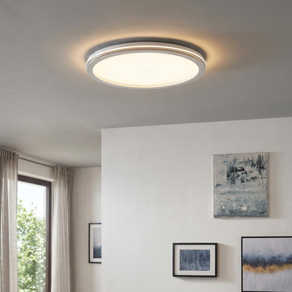 Round white LED flush ceiling light illuminating a modern room with white walls and abstract paintings.