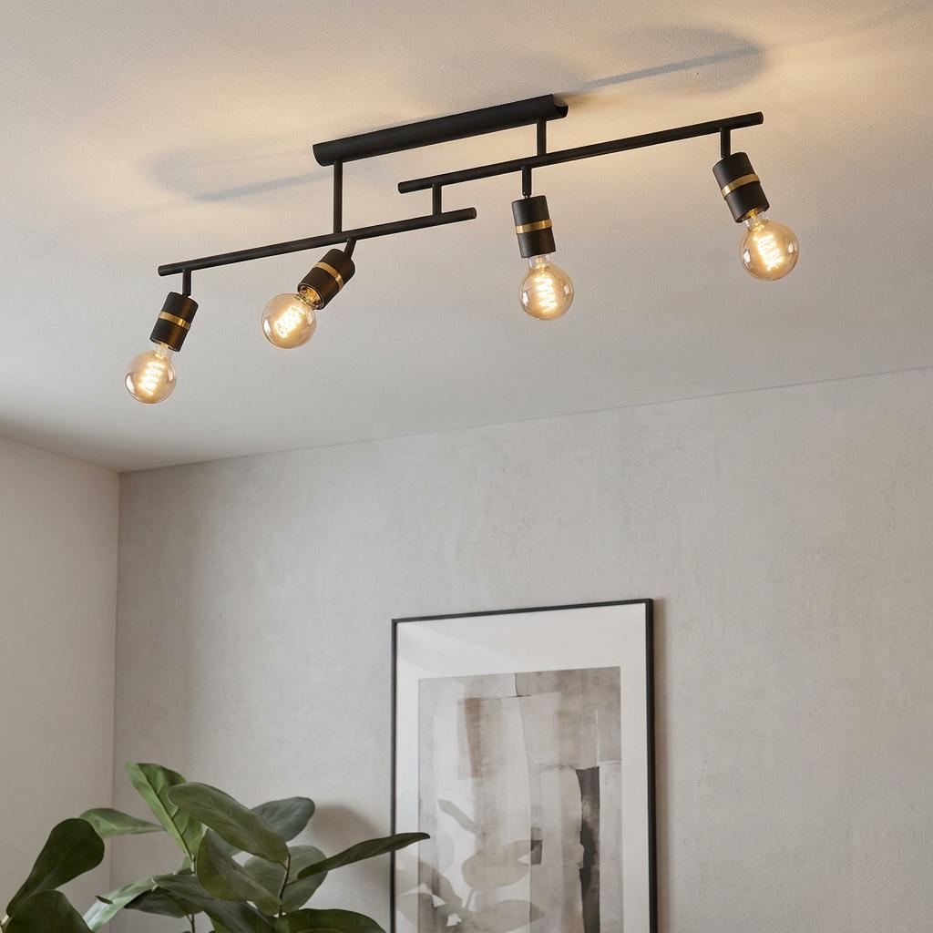 Modern black and brass four-light bar semi-flush ceiling fixture with exposed filament bulbs in a minimalist room.