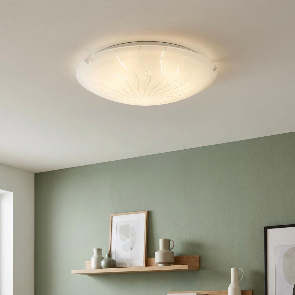 Round white glass flush ceiling light with shimmering swirl pattern mounted above a shelf on a sage green wall.