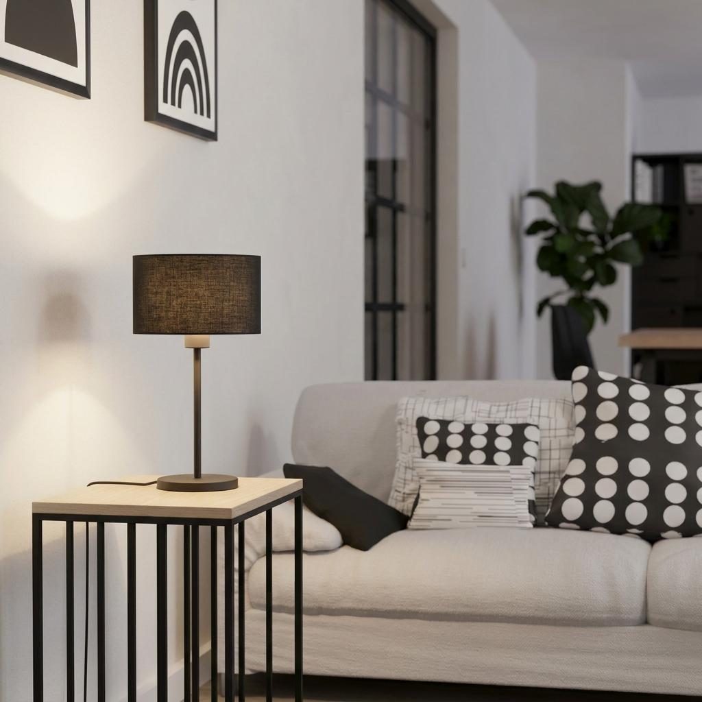 A black table lamp with a fabric shade on a modern side table next to a white sofa in a minimalist living room.