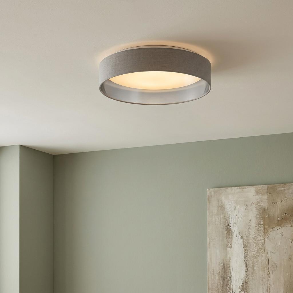 Round grey fabric flush ceiling light with a silver interior glowing warmly on a white ceiling.