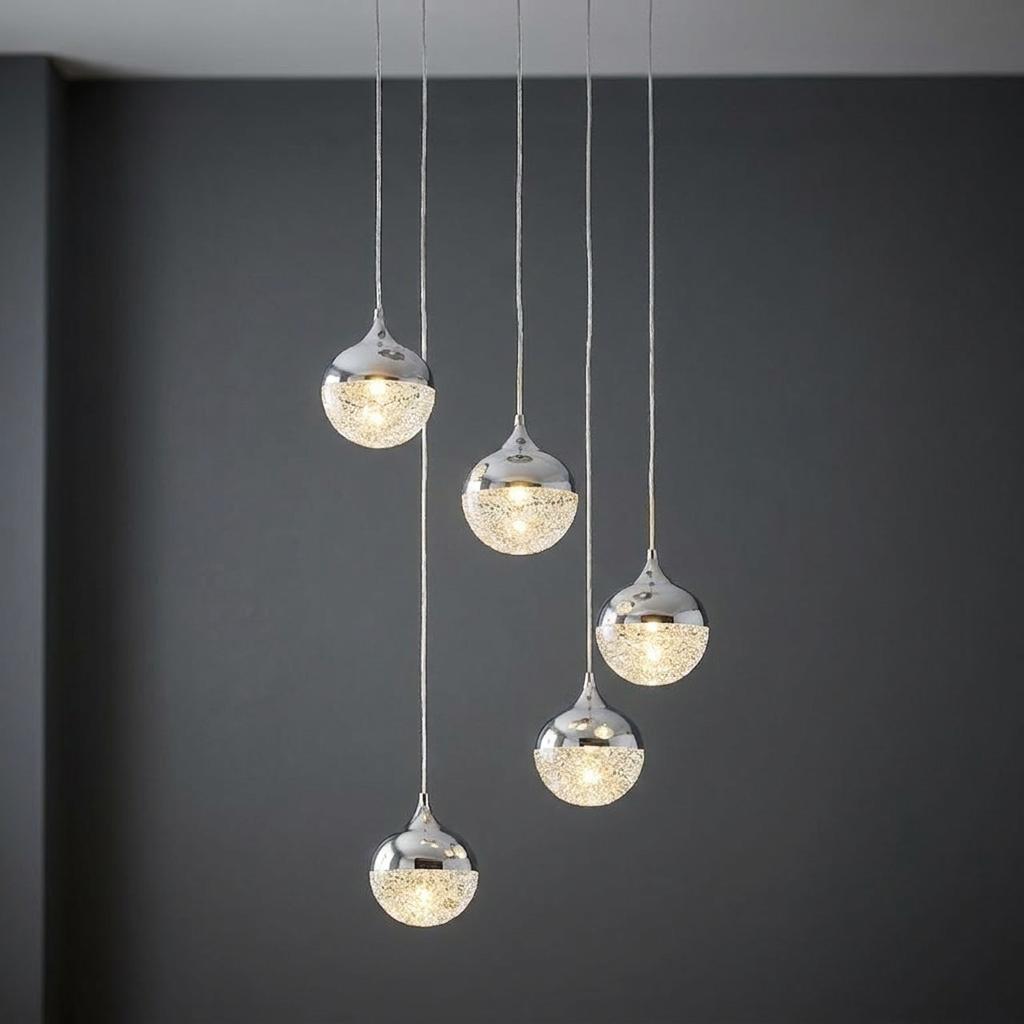 Staggered five-light pendant with polished chrome and sparkling crystal-effect globes against a dark wall.
