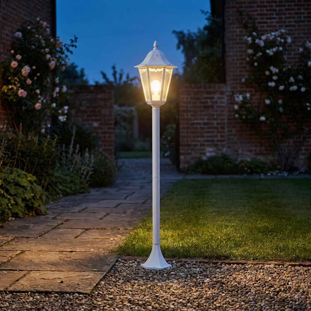 White traditional outdoor lantern post light illuminating a garden stone path and lawn at night.