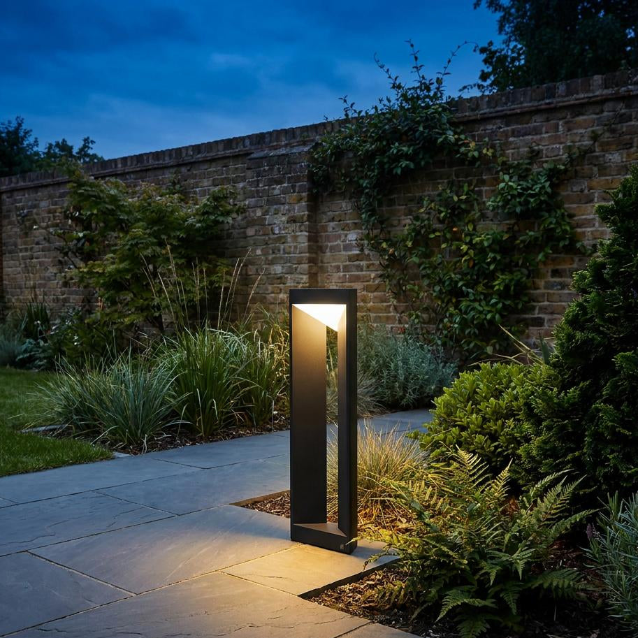 Black linear LED bollard light illuminating a stone garden path next to a brick wall at night.
