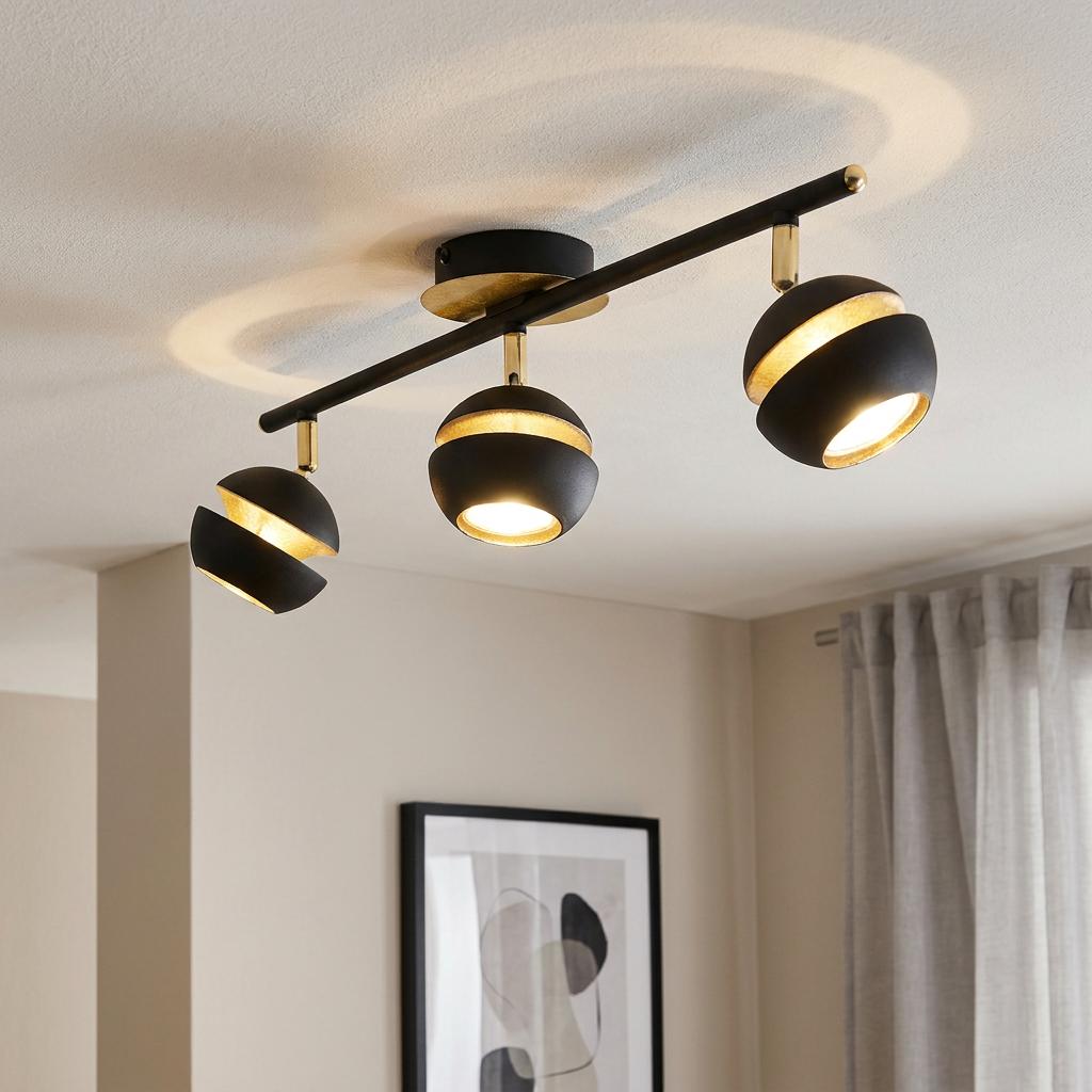 Three-light black and gold bar spotlight mounted on a white ceiling.