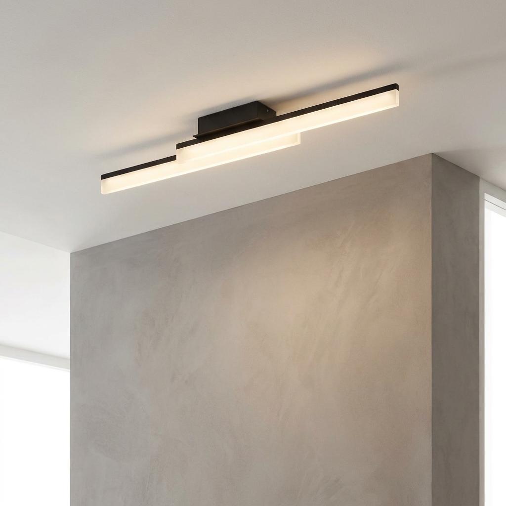 Modern black linear LED flush ceiling light with stepped diffusers mounted on a white ceiling above a grey wall.