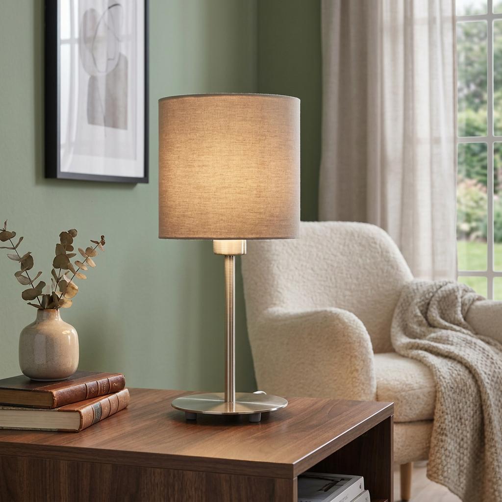Eglo Pasteri table lamp with a taupe fabric shade and nickel base glowing on a wooden side table in a living room.