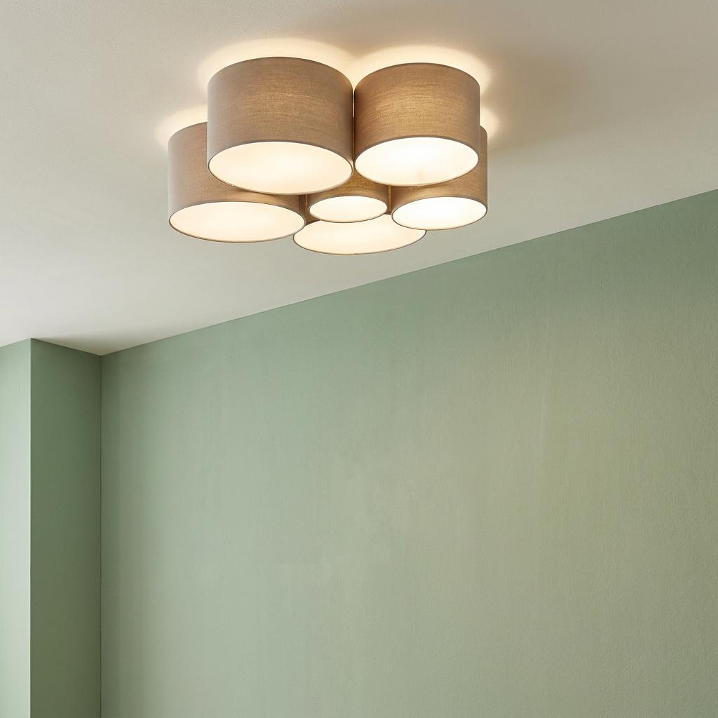 Six taupe fabric drum shades of varying sizes form a flush ceiling light against a pale green wall.