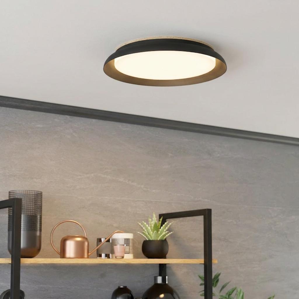 Modern black round LED ceiling flush light with wood accent mounted above a decorative shelf on a grey tiled wall.