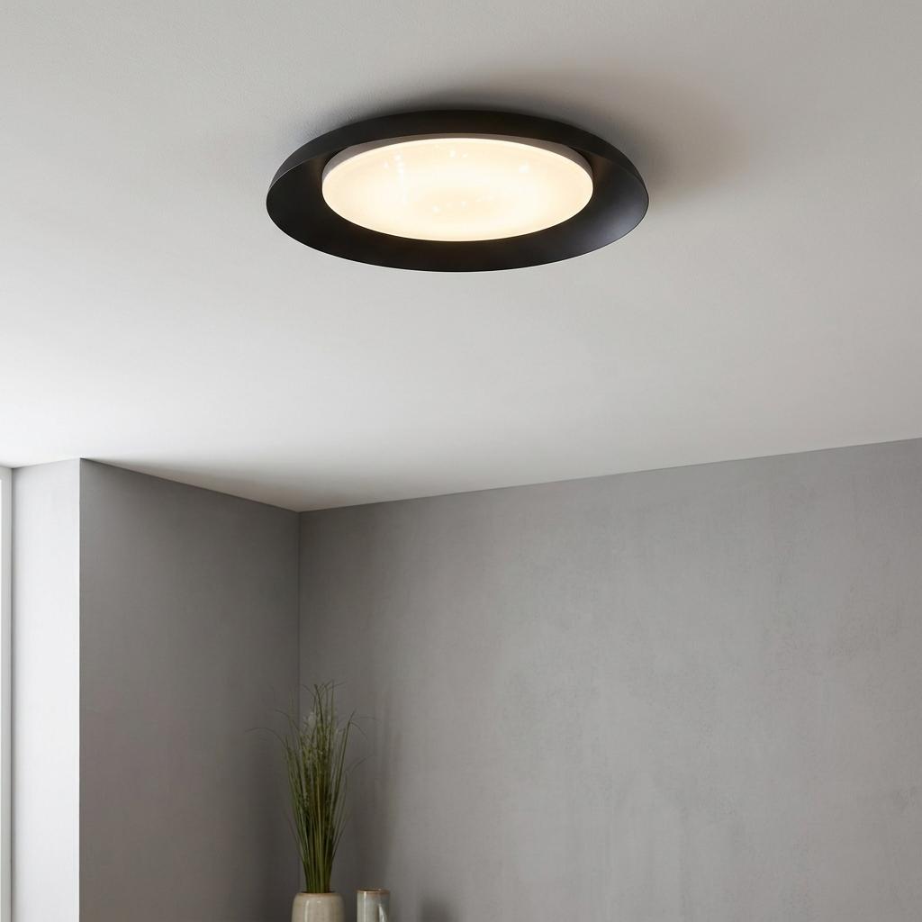 Round black LED flush ceiling light with a warm glowing white diffuser mounted on a clean white ceiling.