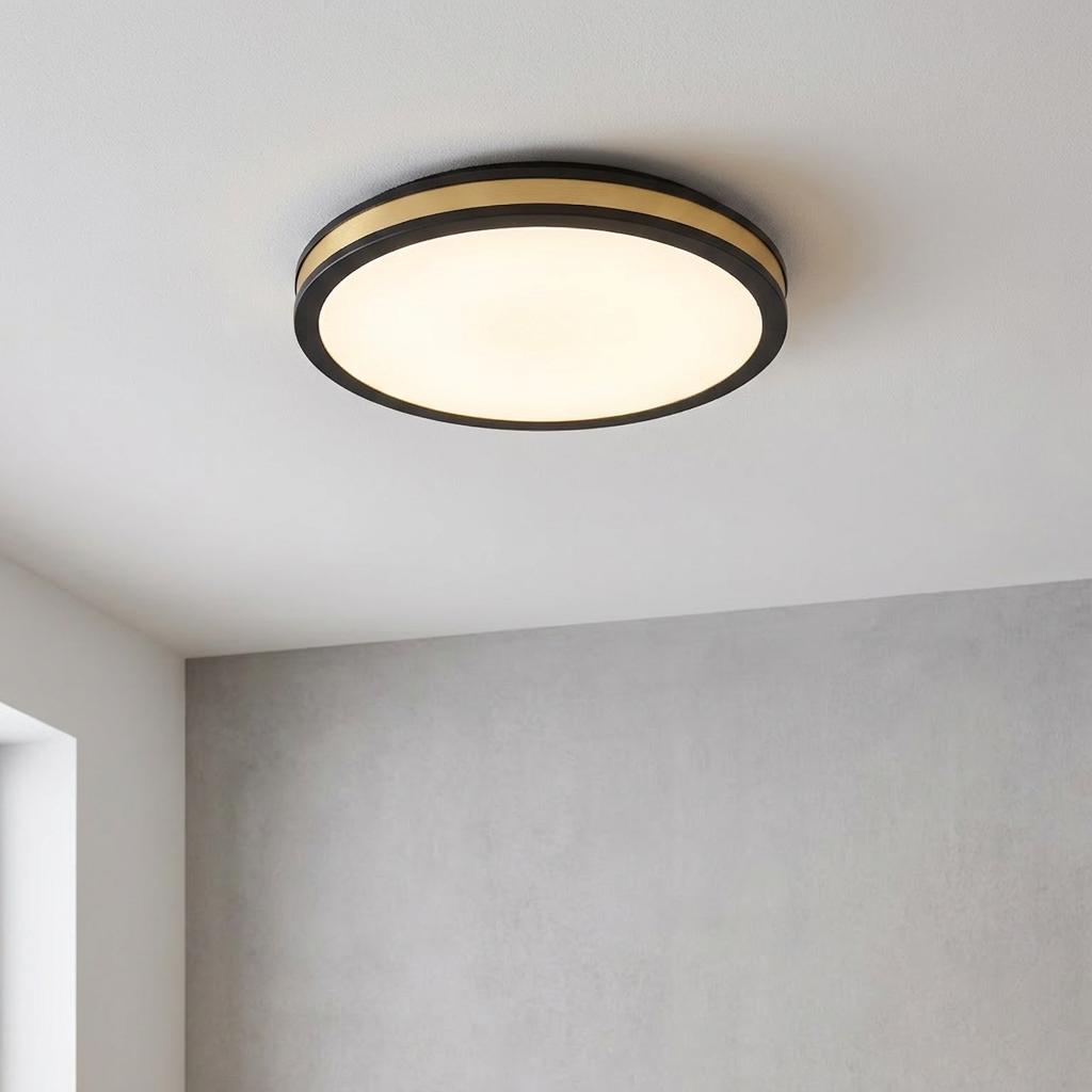 Modern black and gold round flush LED ceiling light emitting warm light in a minimalist room.
