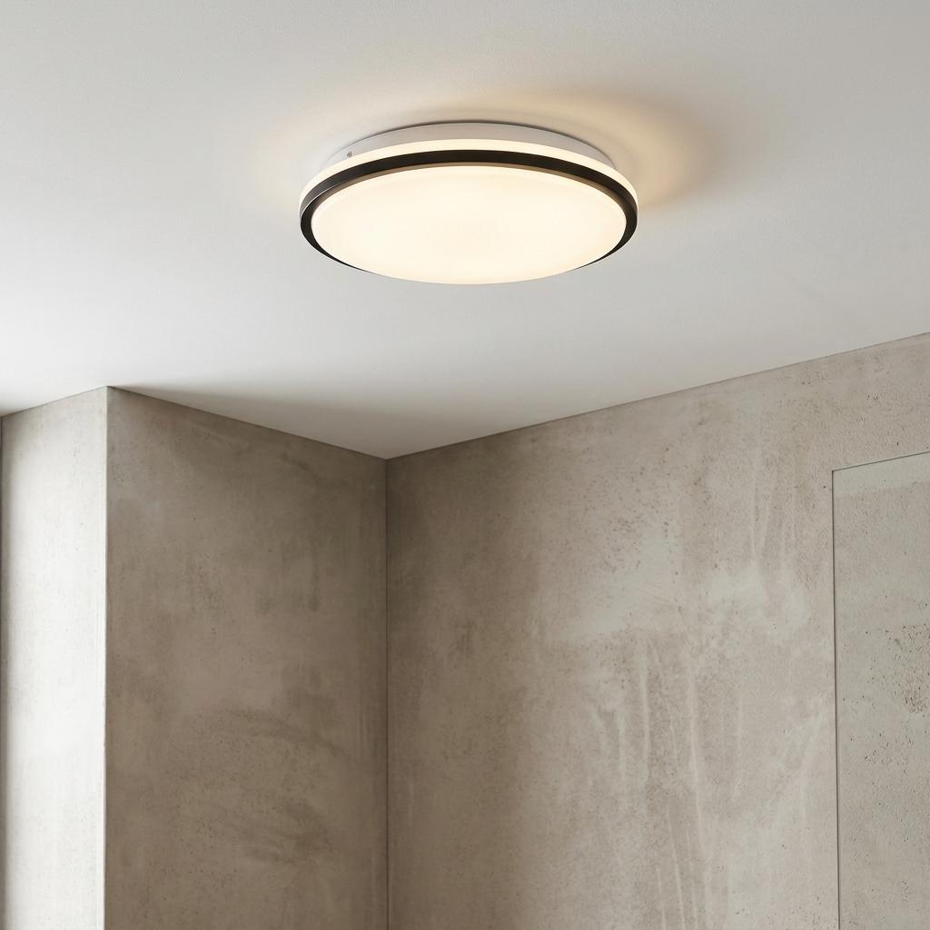 Round black and white LED flush ceiling light glowing in a modern room with grey concrete-textured walls.