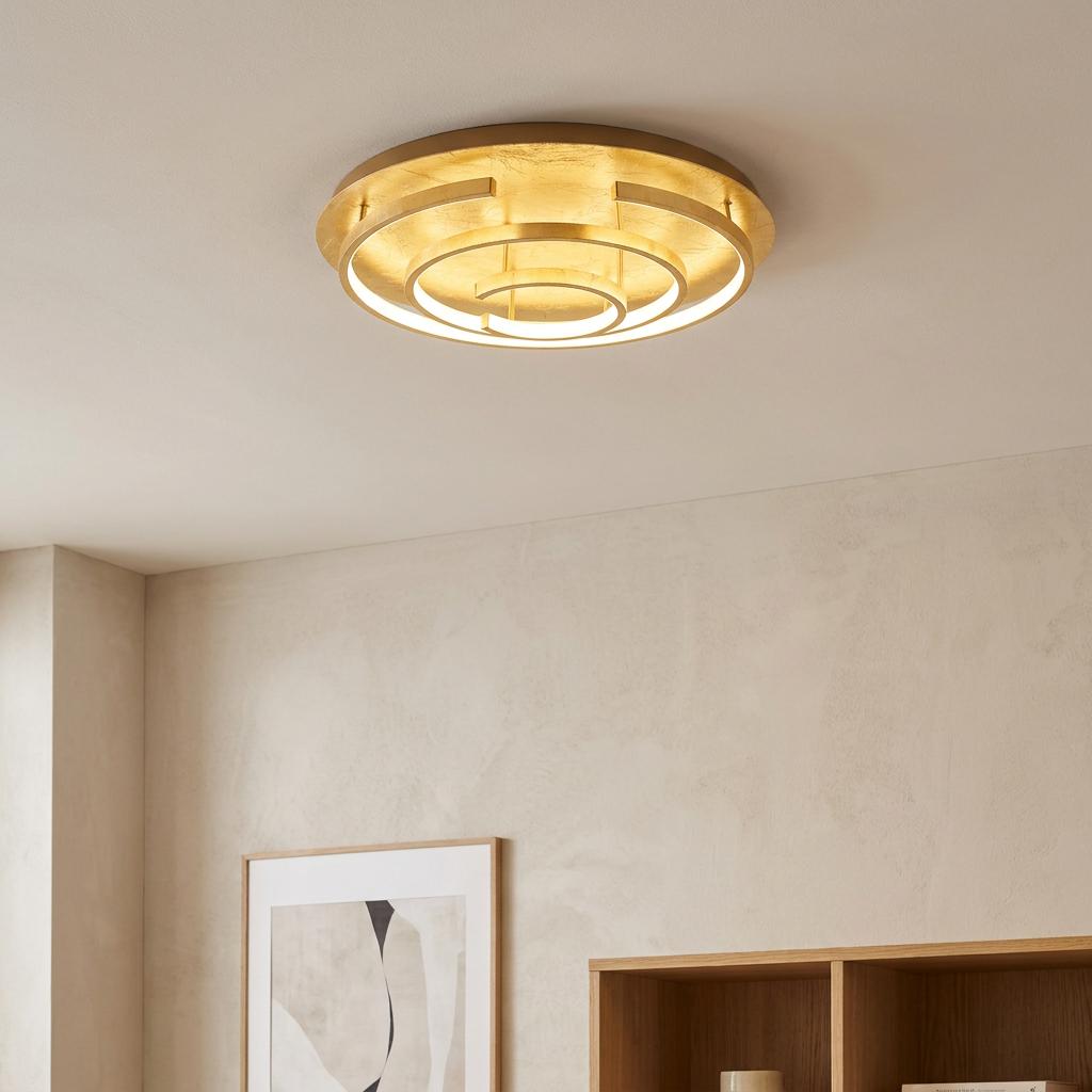 A modern gold leaf flush ceiling light with concentric LED rings illuminating a neutral-toned room.