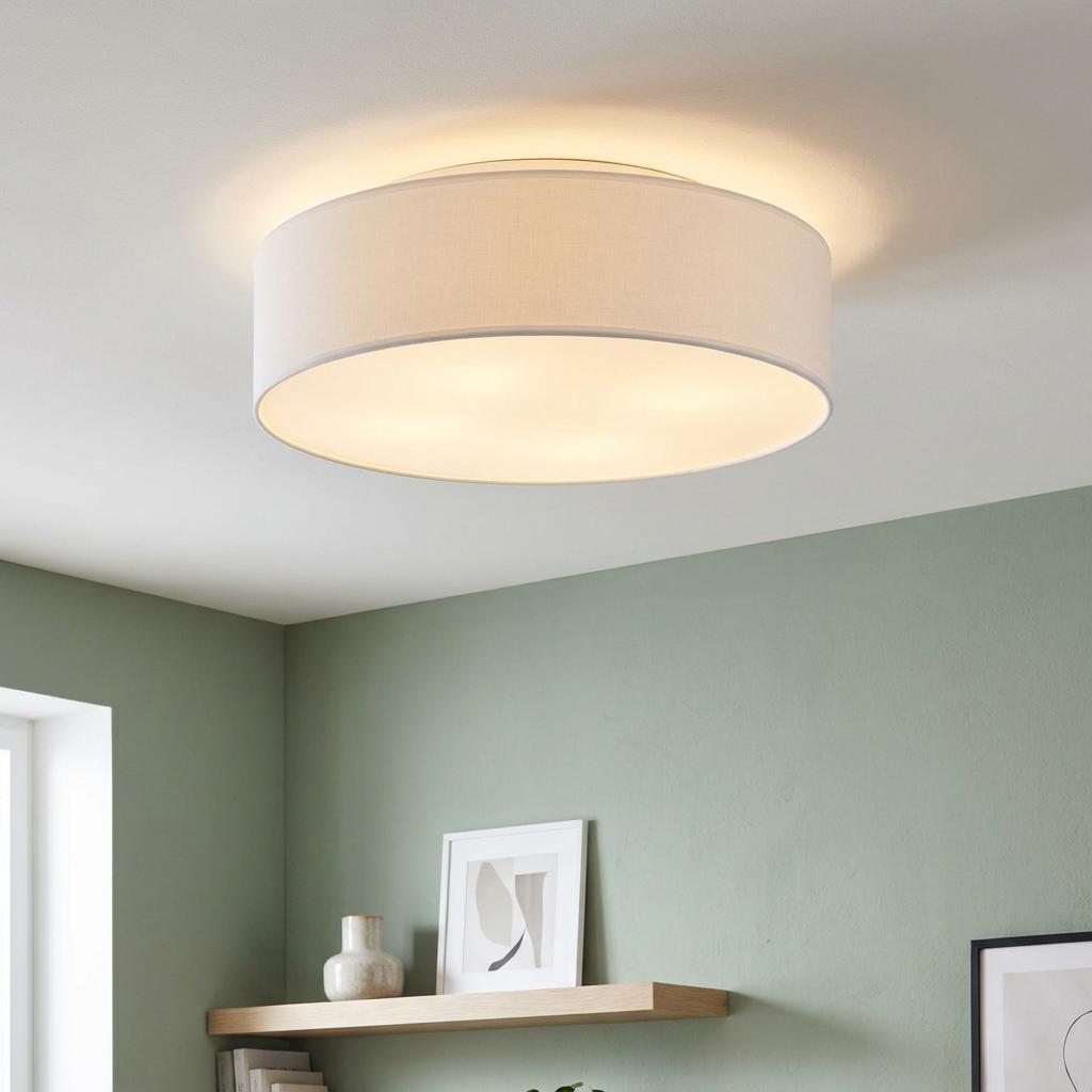 White fabric drum shade flush LED ceiling light illuminated in a modern room with sage green walls.