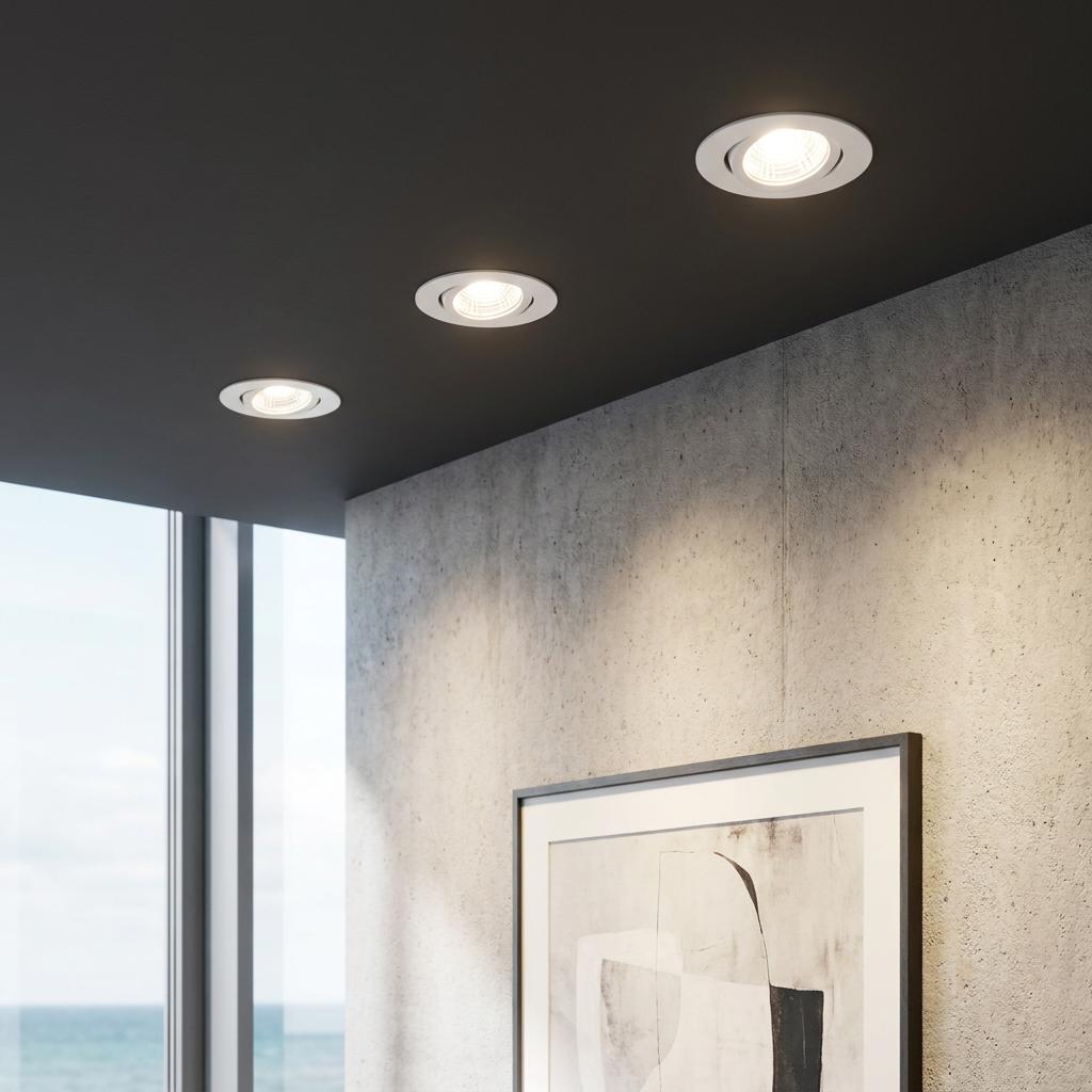 Three warm white LED recessed downlights set in a dark gray ceiling above a concrete wall and framed artwork.