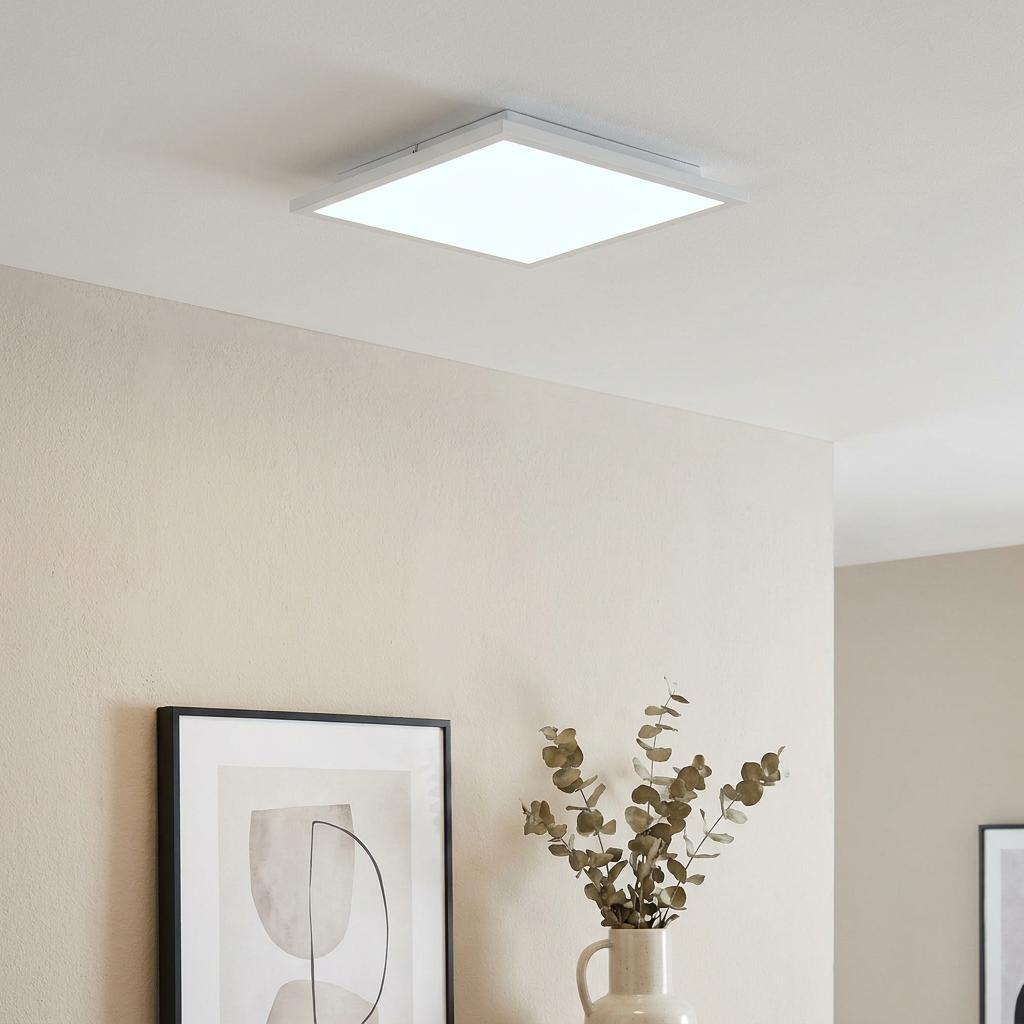 Modern square white LED panel light flush-mounted on a ceiling in a minimalist living space.