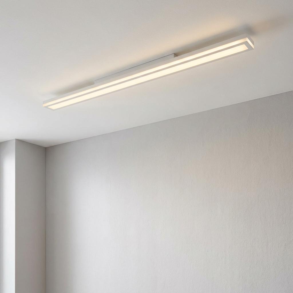 A long, slim white rectangular LED panel flush ceiling light glowing in a minimalist room.