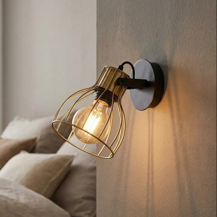 Eglo Sambatello brass wire wall spotlight with an illuminated vintage bulb, mounted on a grey wall in a bedroom.