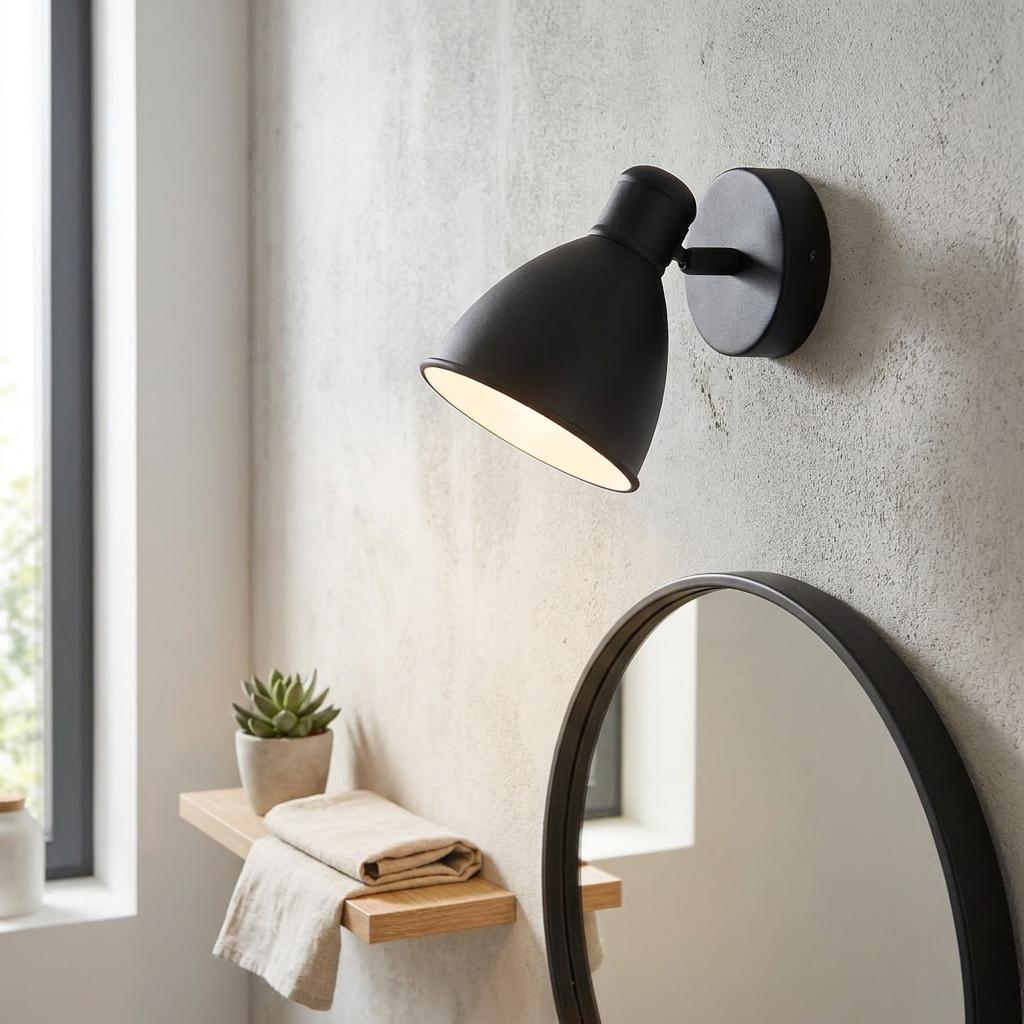 Matte black wall-mounted spotlight illuminating a bathroom wall above a round mirror and a small wooden shelf.