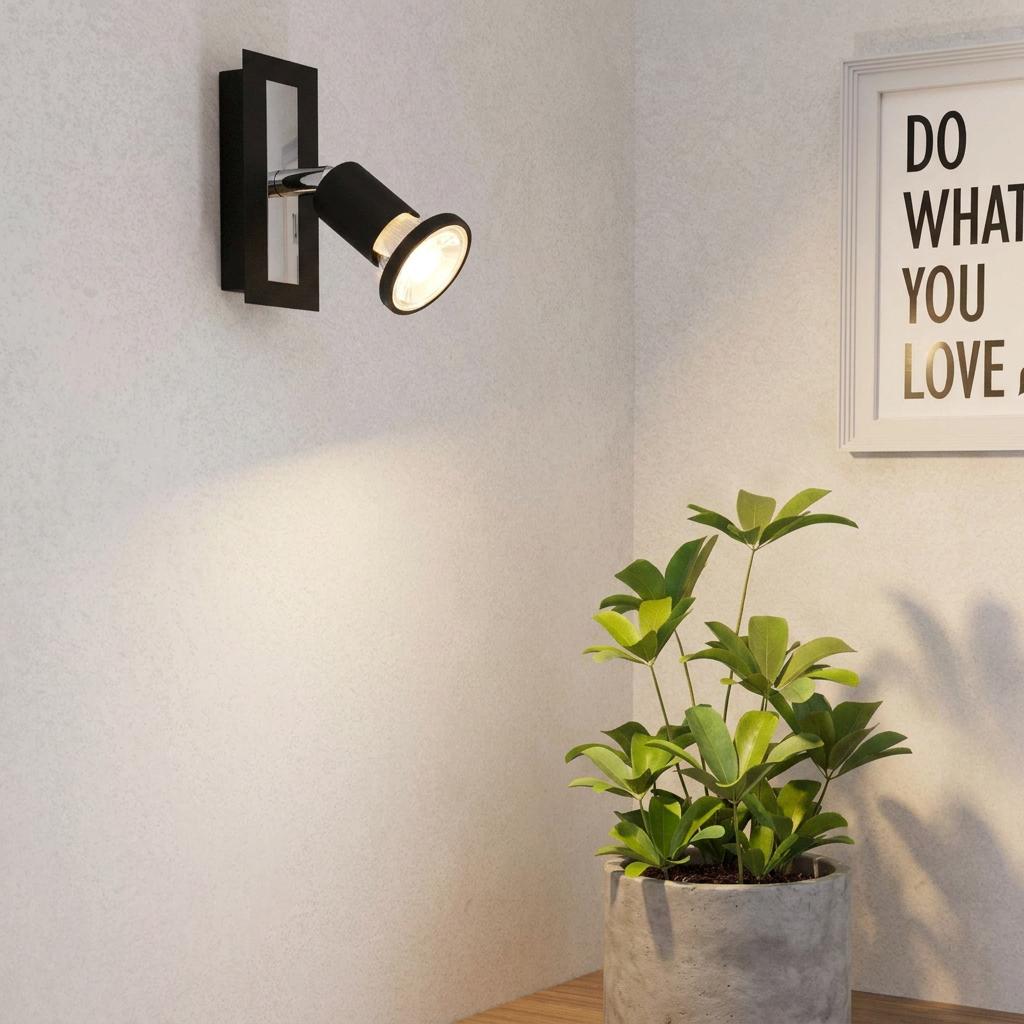 Black and chrome wall spotlight casting a warm glow on a potted plant in a minimalist room.