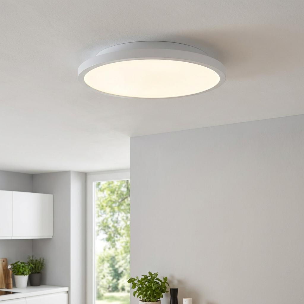 Minimalist white circular LED ceiling light illuminated against a white ceiling in a clean, modern room.