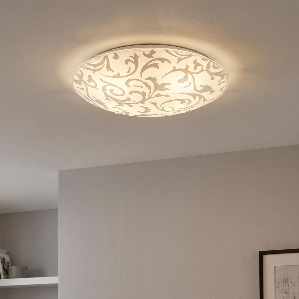Circular flush ceiling light with a white floral scroll pattern on satin glass, emitting a warm glow.