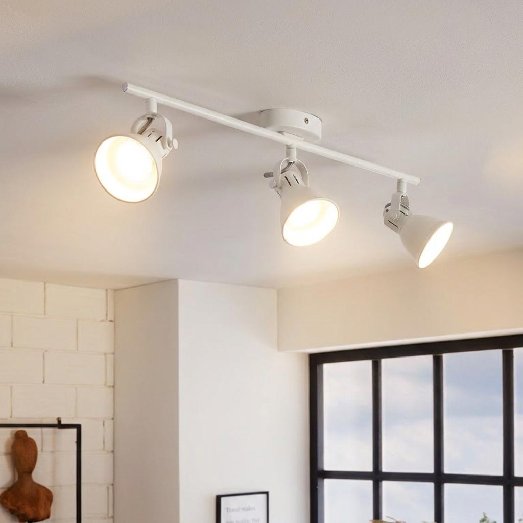 Three-light white bar spotlight fixture illuminated on a white ceiling in a bright, modern interior.