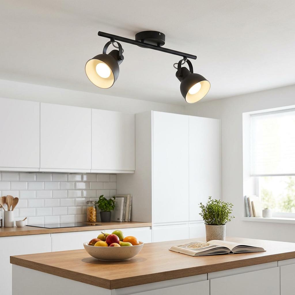 Black two-light bar spotlight mounted on a kitchen ceiling, illuminating a modern kitchen island with warm light.