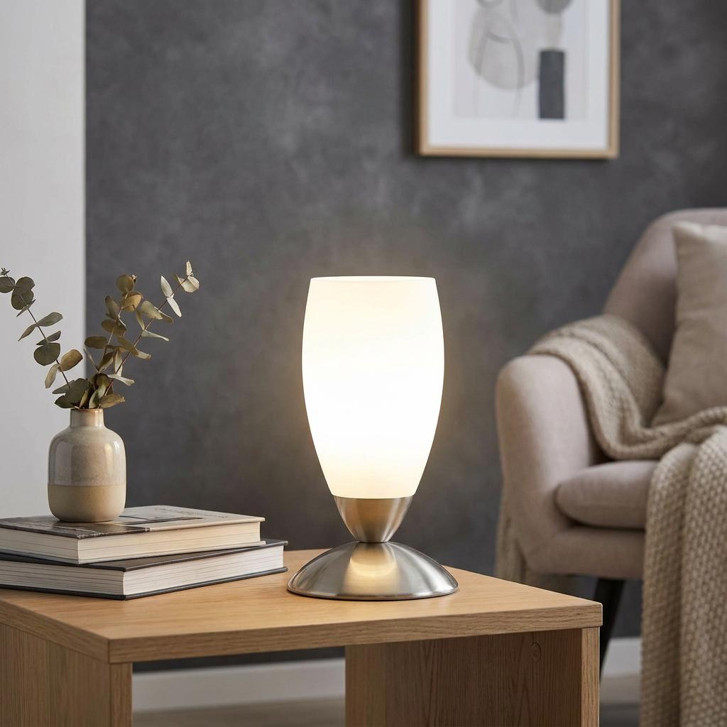 Lit Eglo Slim table lamp with satin glass shade and nickel base on a wooden side table in a living room.