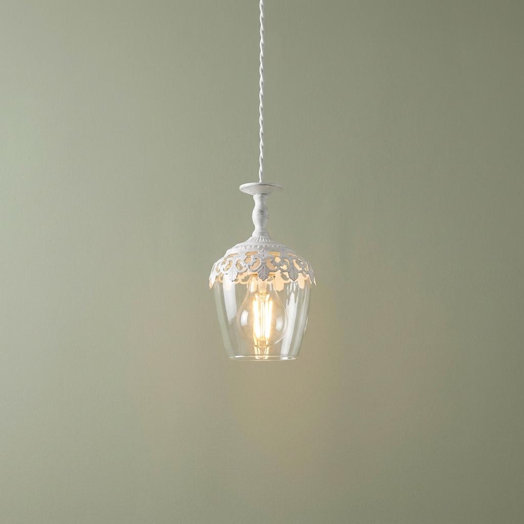 Vintage-style white metal and glass pendant light with intricate scrollwork hanging against a plain green wall.