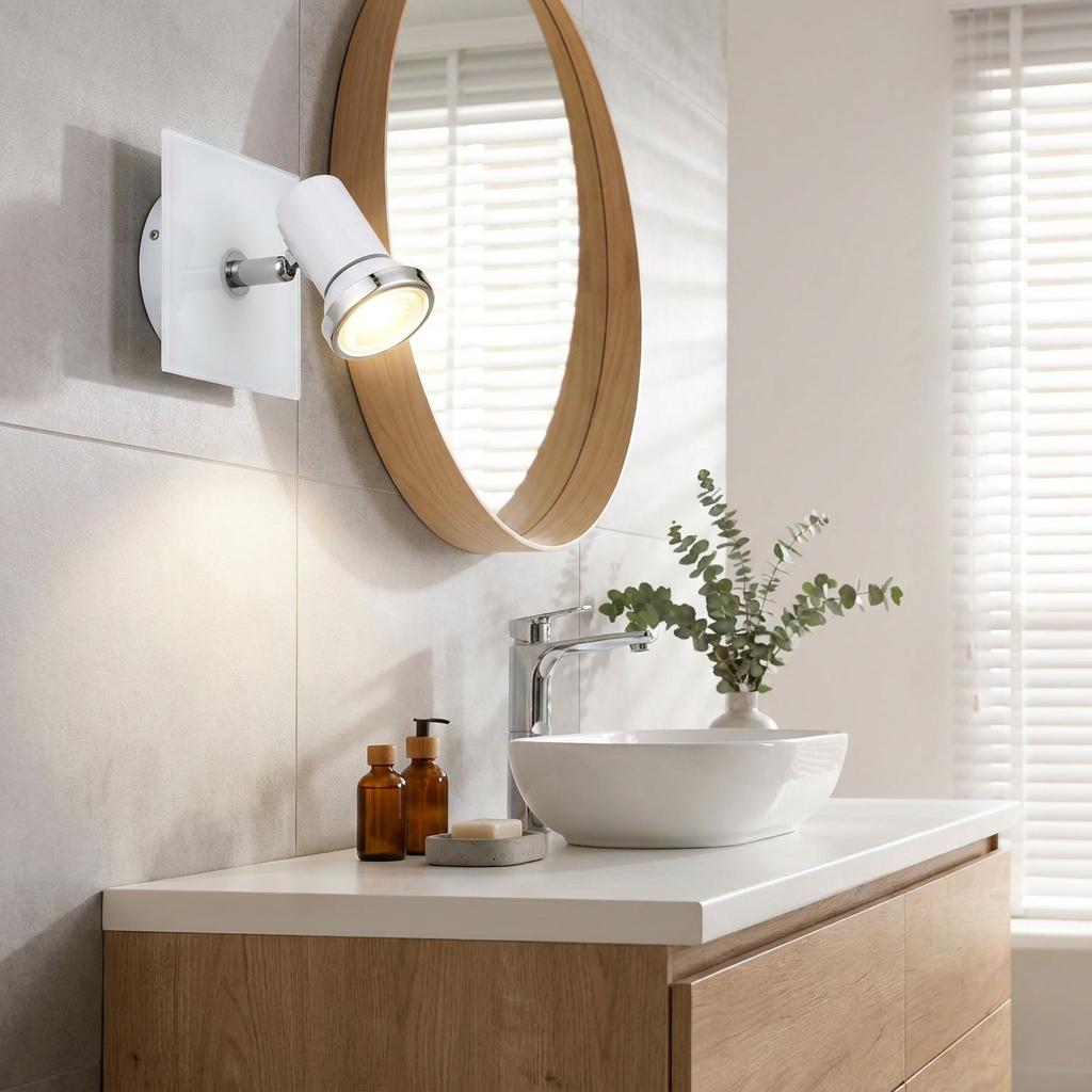 White and chrome bathroom wall spotlight mounted on a tiled wall above a wooden vanity and vessel sink.