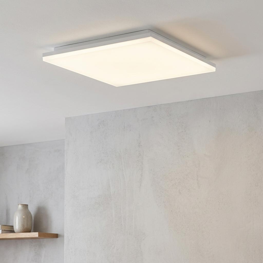 Square white LED flush mount ceiling light illuminating a minimalist room with a grey textured wall.