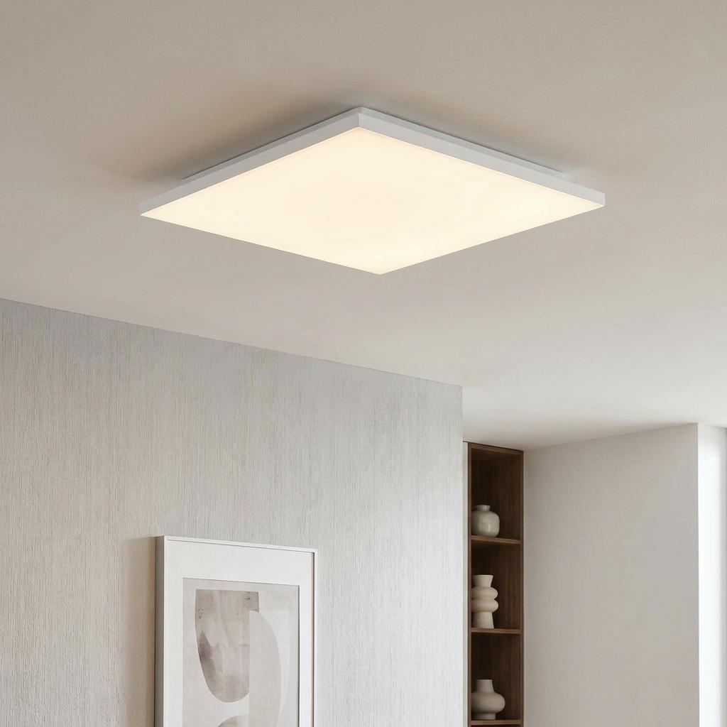 Square white LED flush mount ceiling light illuminating a modern room with a neutral wall and framed art.