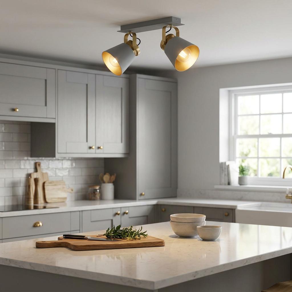 A two-light grey and gold bar spotlight fixed to a kitchen ceiling, illuminating a modern grey kitchen island.