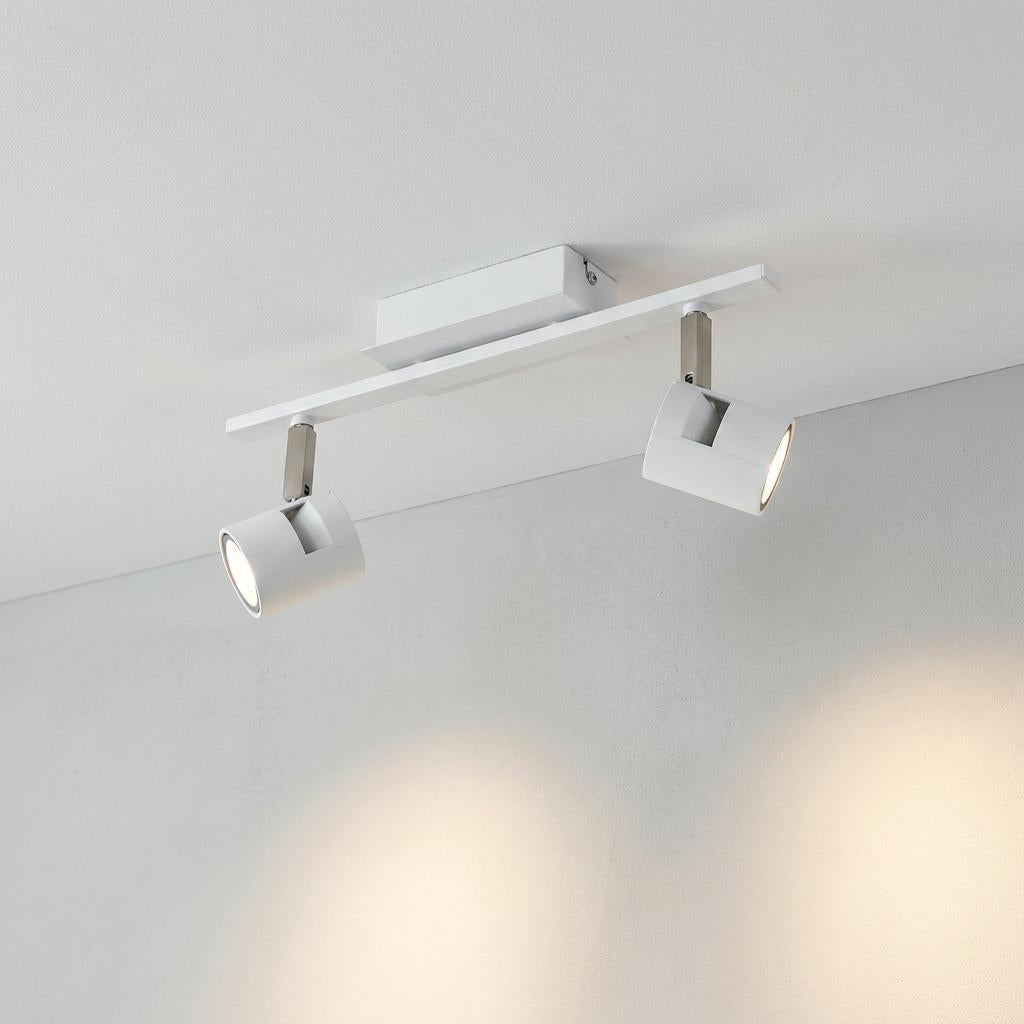 Modern white 2-light bar spotlight fixed to a ceiling, casting warm light on a plain wall.