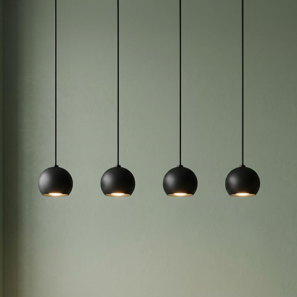 Four matt black spherical pendant lights hanging in a row against a sage green wall, emitting a warm downward glow.