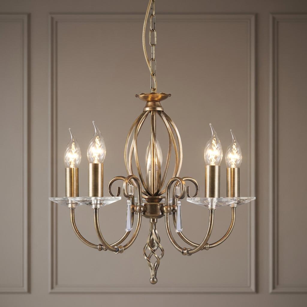 Elstead Aegean 5 light chandelier in aged brass with curved arms and glass droplets against a panelled wall.