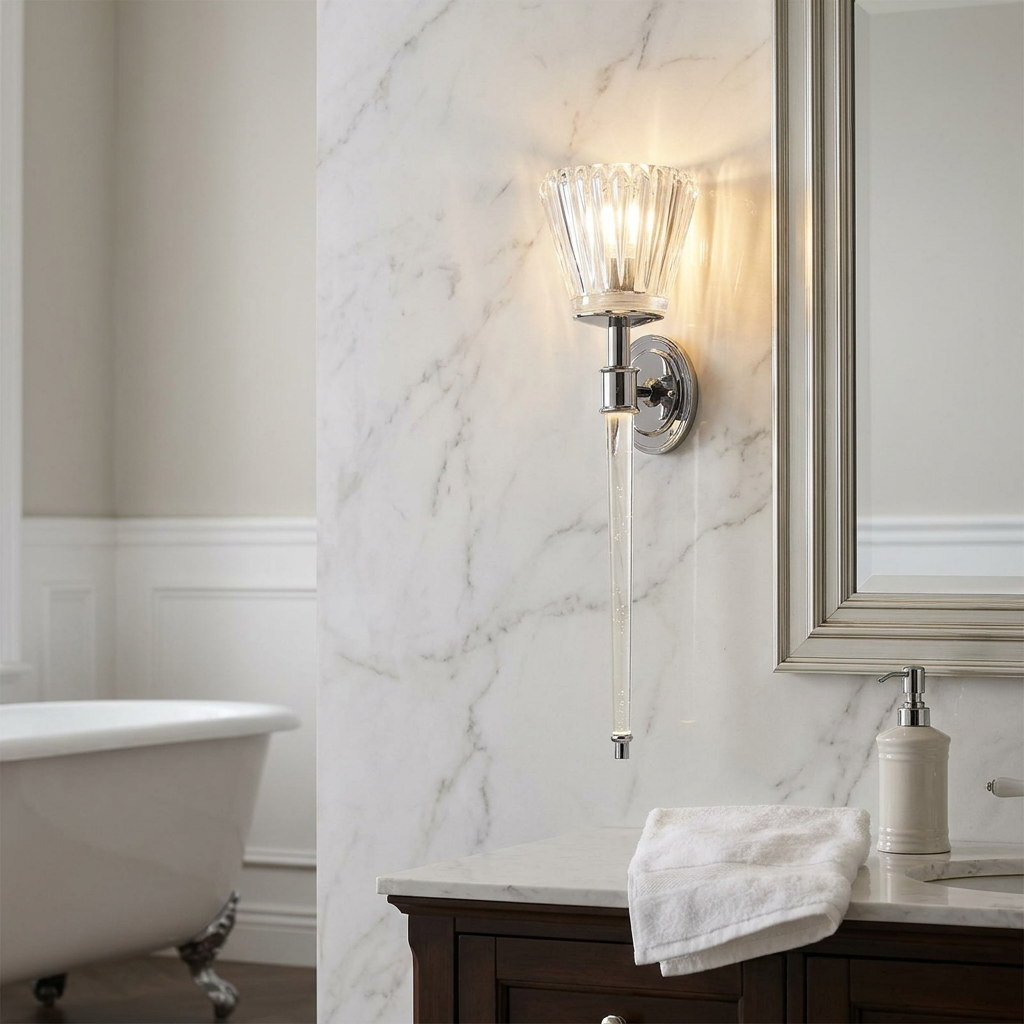Elegant polished chrome wall sconce with a fluted glass shade and long clear rod mounted on a marble bathroom wall.